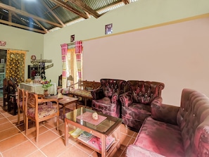 A living room with a leather sofa, a glass coffee table, and a dining area with a table set for two. - OYO Homes 91118 Homesstay Desa Wisata Budo (Wori)