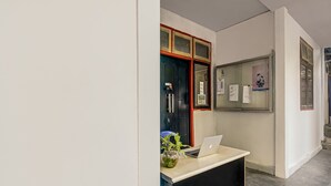 Un comptoir d’accueil avec un ordinateur portable, un vase de fleurs et un tableau d’affichage où sont accrochés des documents.