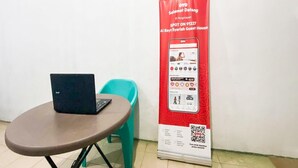 A laptop on a table, a QR code on a red poster, and a teal chair. - Spot ON 91227 Al Bayt Syariah Guest House (Kupang)