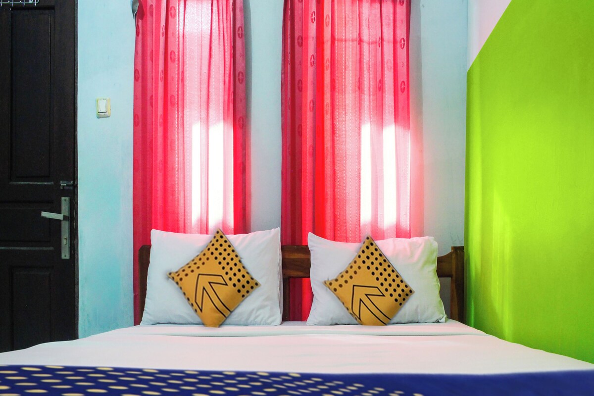 A bed with two pillows, a door, and a window with red curtains.