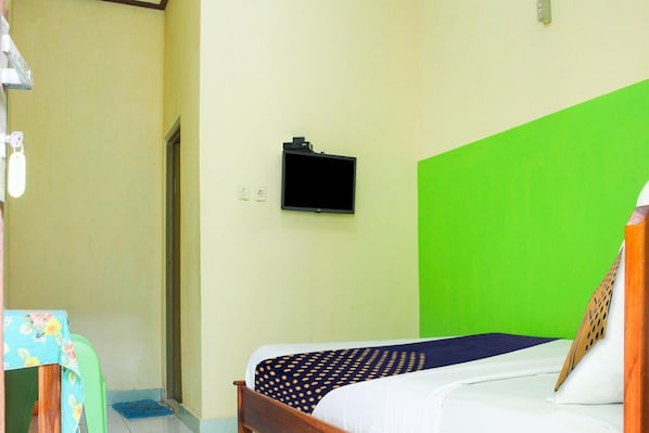 Une pièce avec un lit, un mur vert, un téléviseur fixé au mur et une porte.