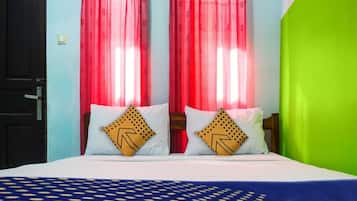 A bed with two pillows, a patterned bedspread, and red curtains.