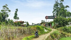 Un camino rural con una motocicleta estacionada al borde, rodeado de vegetación y un letrero que indica una zona local.