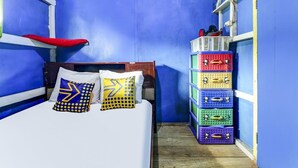 Una habitación estrecha con una cama, almohadas y coloridos contenedores para guardar objetos.