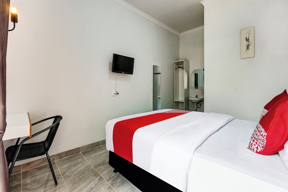 Una habitación de hotel con cama, televisión montada en la pared, armario y escritorio con silla.