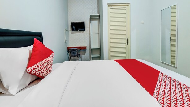 A hotel room with a bed, a TV mounted on the wall, a wardrobe, and a mirror. - OYO Flagship 90983 Harmony Easy Stay (Depok)