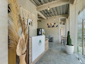 A reception area with a modern design, including a reception desk, a sofa, and a cactus plant. - OYO Flagship 90983 Harmony Easy Stay (Depok)
