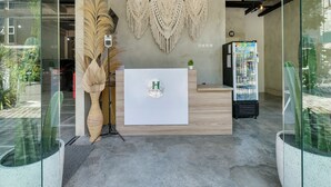 A reception area with a wooden reception desk, a wall-mounted macrame decoration, a refrigerator, and potted plants. - OYO Flagship 90983 Harmony Easy Stay (Depok)