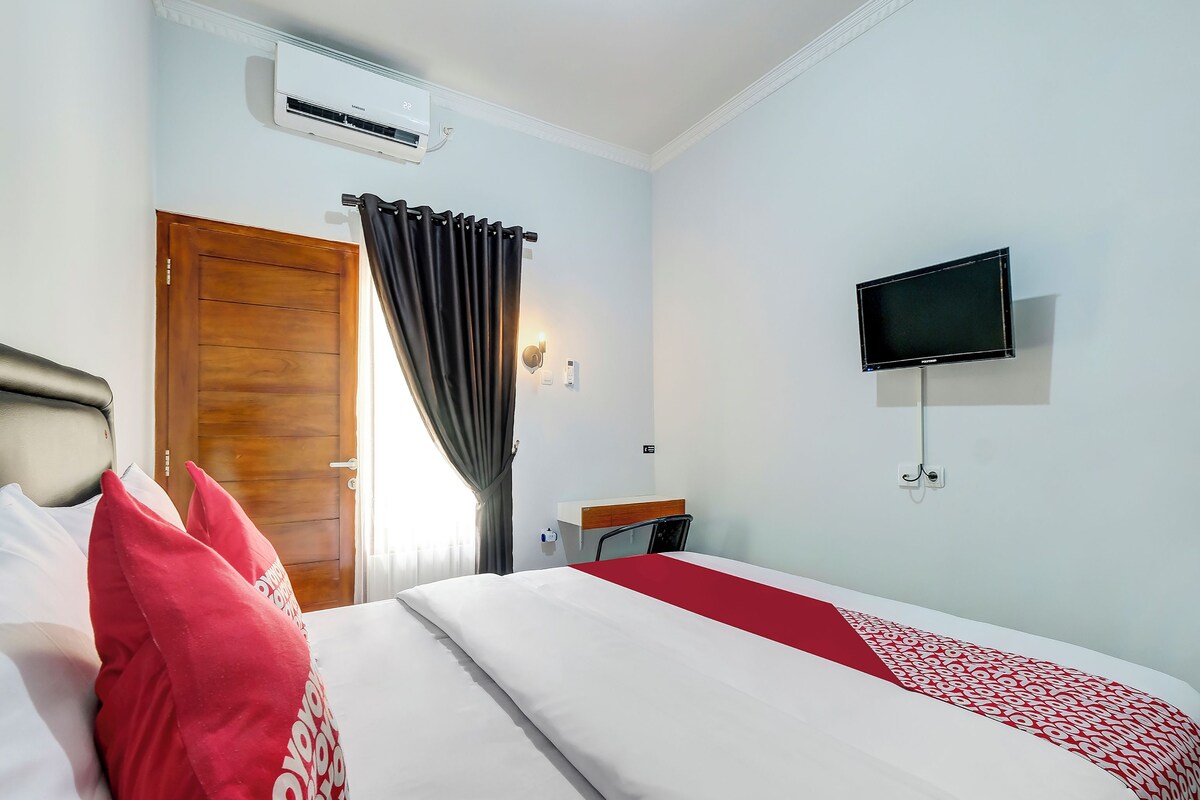 A hotel room with a bed, a TV, and a window with curtains.