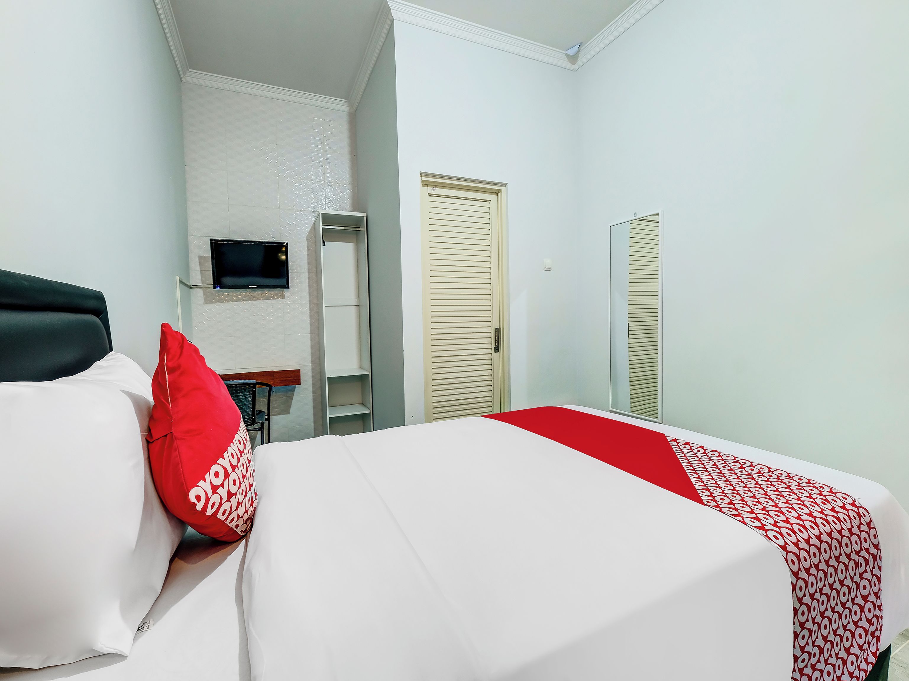 A hotel room with a bed, a TV mounted on the wall, a wardrobe, and a mirror.