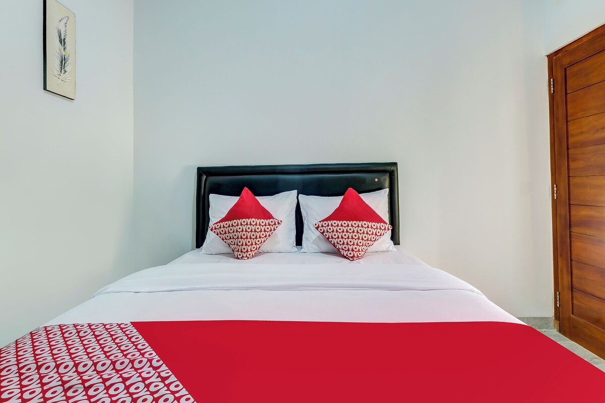 Ein Bett mit einer Bettdecke in Weiß und Rot mit Muster, zwei rote Kissen mit einem sich wiederholenden Muster und ein gerahmtes Bild an der Wand.