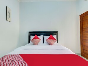 A bed with a white and red patterned bedspread, two red pillows with a repeated pattern, and a framed picture on the wall. - OYO Flagship 90983 Harmony Easy Stay (Depok)