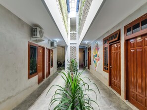 A corridor with wooden doors, a central air conditioning unit, and a ceiling with a skylight. - OYO Flagship 90983 Harmony Easy Stay (Depok)