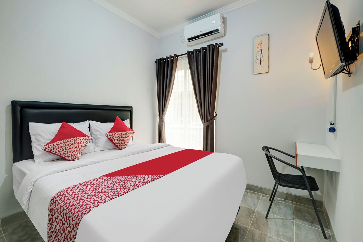 Ein Hotelzimmer mit Bett, Schreibtisch, Klimaanlage und an der Wand befestigtem Fernseher.