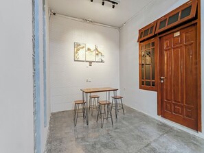 Une pièce avec une table en bois et quatre tabourets, une porte en bois et un luminaire fixé au mur.