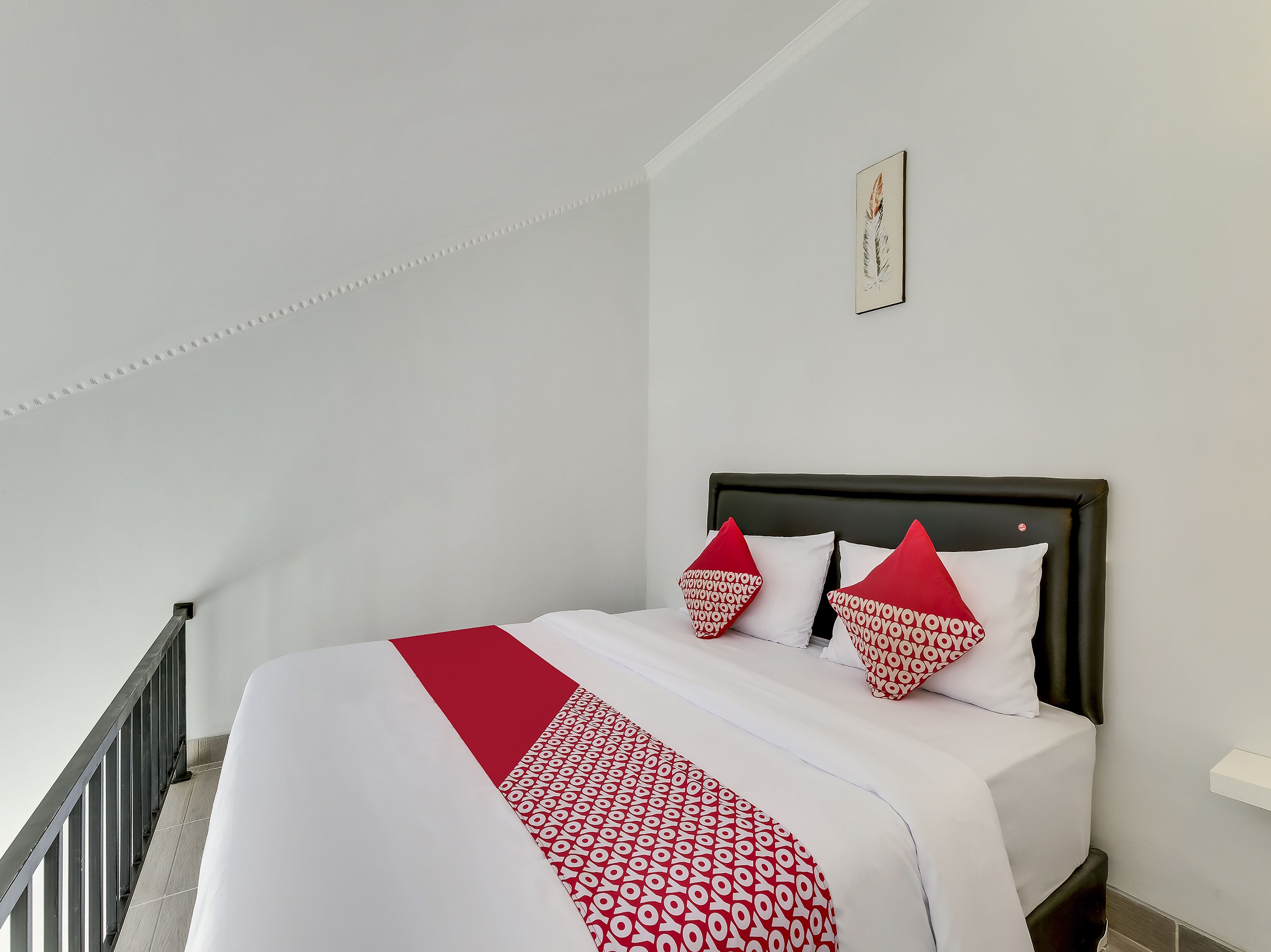 Una cama bien hecha con una colcha blanca y roja estampada, dos almohadas rojas y un cuadro en la pared.