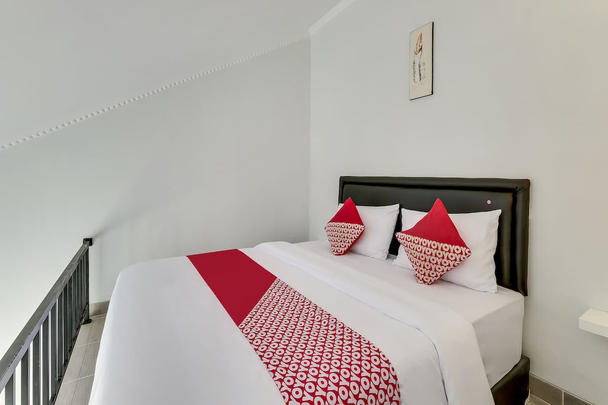 Ein ordentlich bezogenes Bett mit einer Bettdecke in Weiß und Rot, zwei rote Kissen und ein gerahmtes Bild an der Wand.