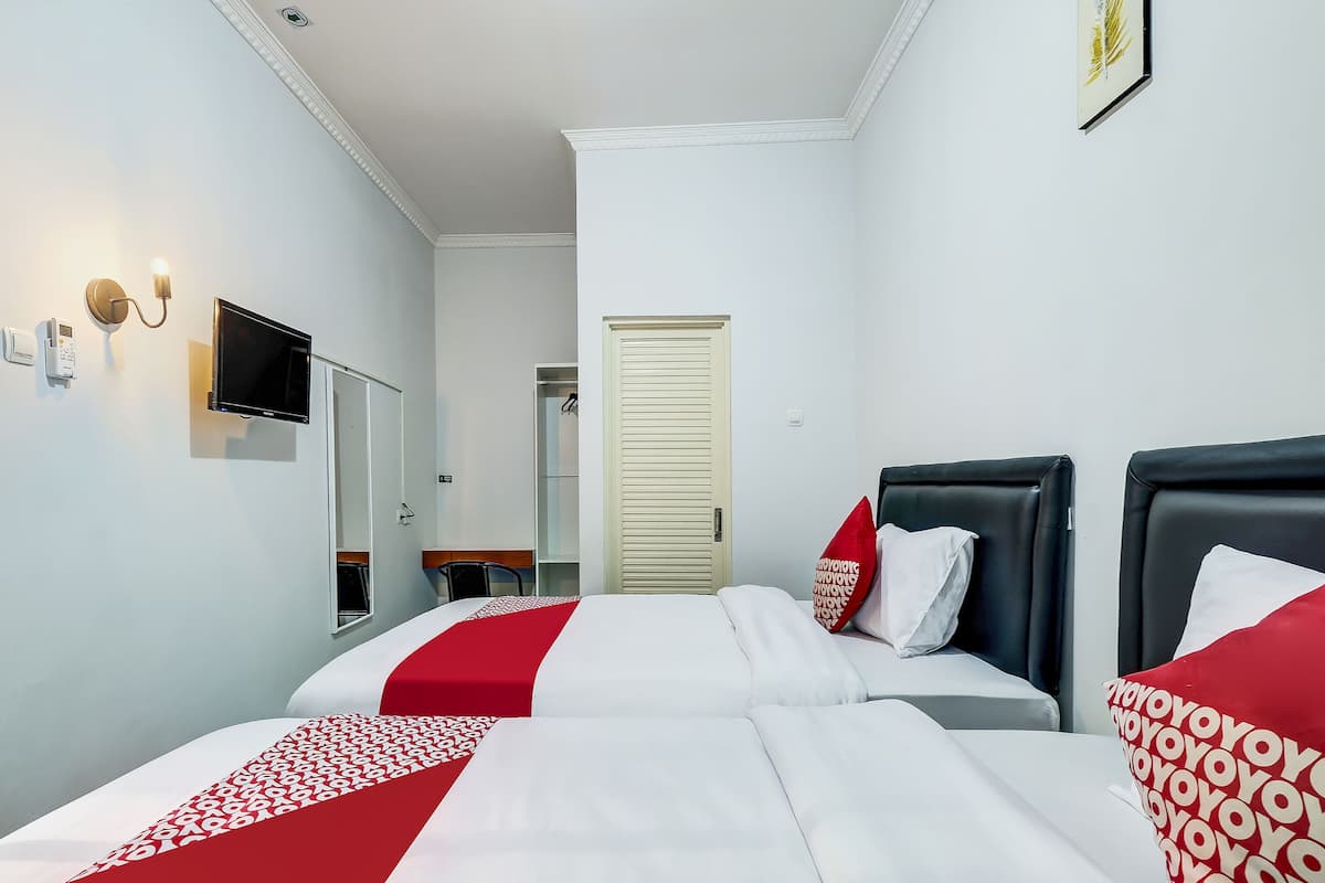 Ein Hotelzimmer mit zwei Betten, einem Fernseher, einem Schreibtisch und einem Kleiderschrank.