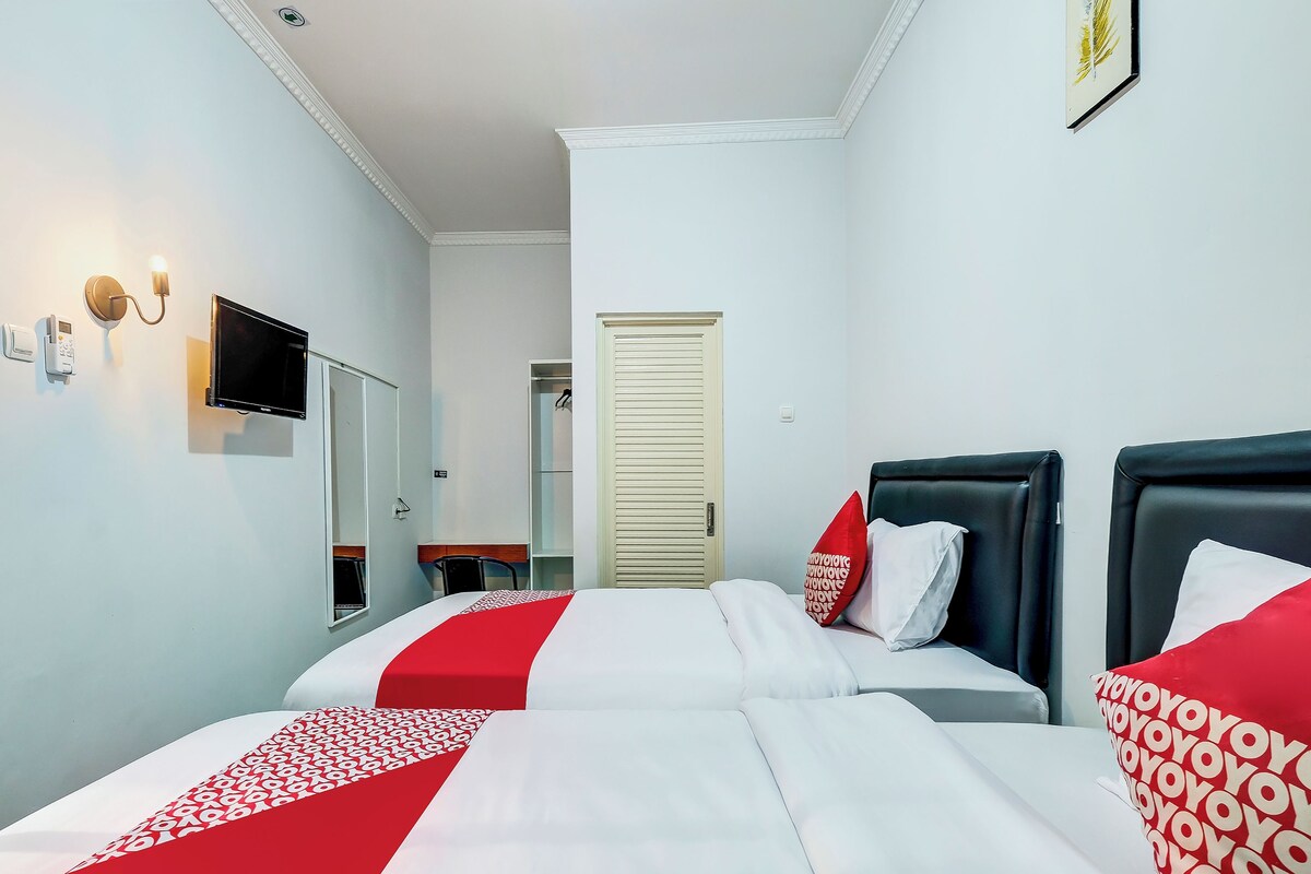 Ein Hotelzimmer mit zwei Betten, einem Fernseher, einem Schreibtisch und einem Kleiderschrank.