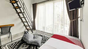 A modern hotel room with a bed, a flat-screen TV, a desk, and a staircase. - OYO Flagship 90983 Harmony Easy Stay (Depok)