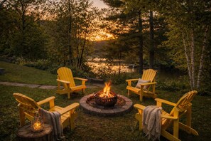 Puutarhamaisessa ympäristössä sijaitsee nuotiopaikka, jonka ympärillä on Adirondack-tyylisiä puutarhatuoleja. Paikalta avautuu näkymä vesistöön ja puustoon.