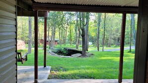 Un patio coperto con pavimento in cemento, pilastri in legno e vista su un prato alberato.
