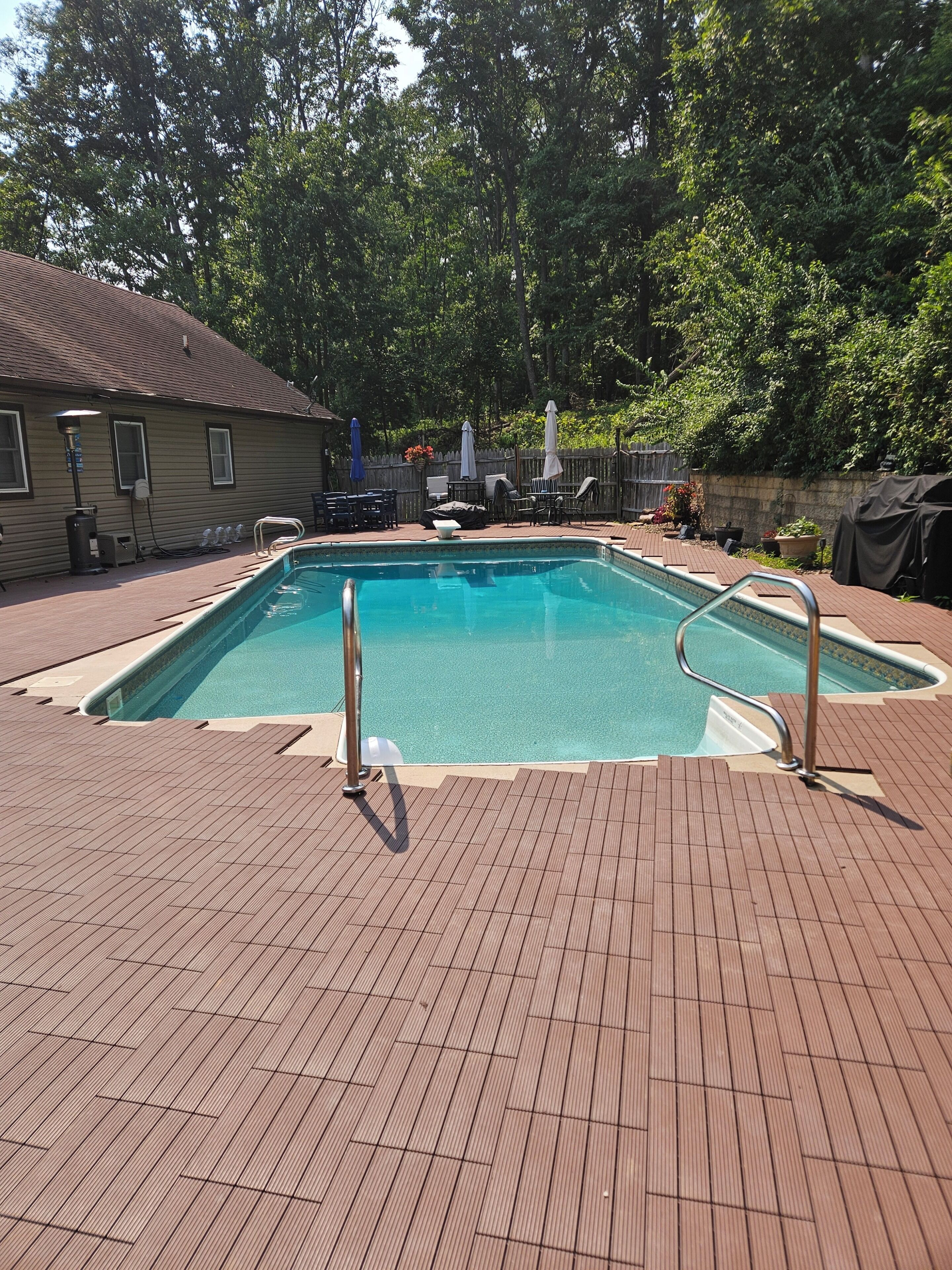 Una piscina rectangular con borde de baldosas, rodeada por un muelle de madera y una cerca de madera.