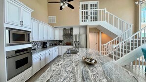 A kitchen with white cabinets, a granite countertop, a microwave, a stove, and a ceiling fan. - License to Chill! Bring Your Boat, Sup or Kayak to this 3 bedroom, 3 bath Waterfront Home - Deep Water Canal, No Bridges. Near golf, shops, restaurants. (Sanibel)