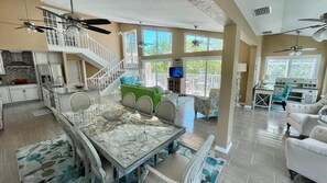 A spacious living area with a high ceiling, multiple ceiling fans, a dining area with a glass-top table, and a balcony with outdoor seating.