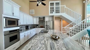 A kitchen with white cabinets, a granite countertop, a microwave, a stove, and a ceiling fan. - License to Chill! Bring Your Boat, Sup or Kayak to this 3 bedroom, 3 bath Waterfront Home - Deep Water Canal, No Bridges. Near golf, shops, restaurants. (Sanibel)