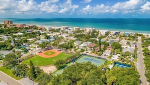 Ett flygbildsfoto av ett bostadsområde vid kusten med en baseballplan, tennisbanor och en strand.