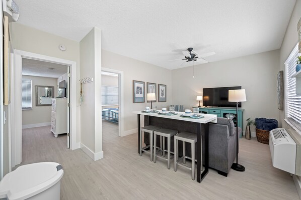A modern kitchen with a dining area, a ceiling fan, and a TV.