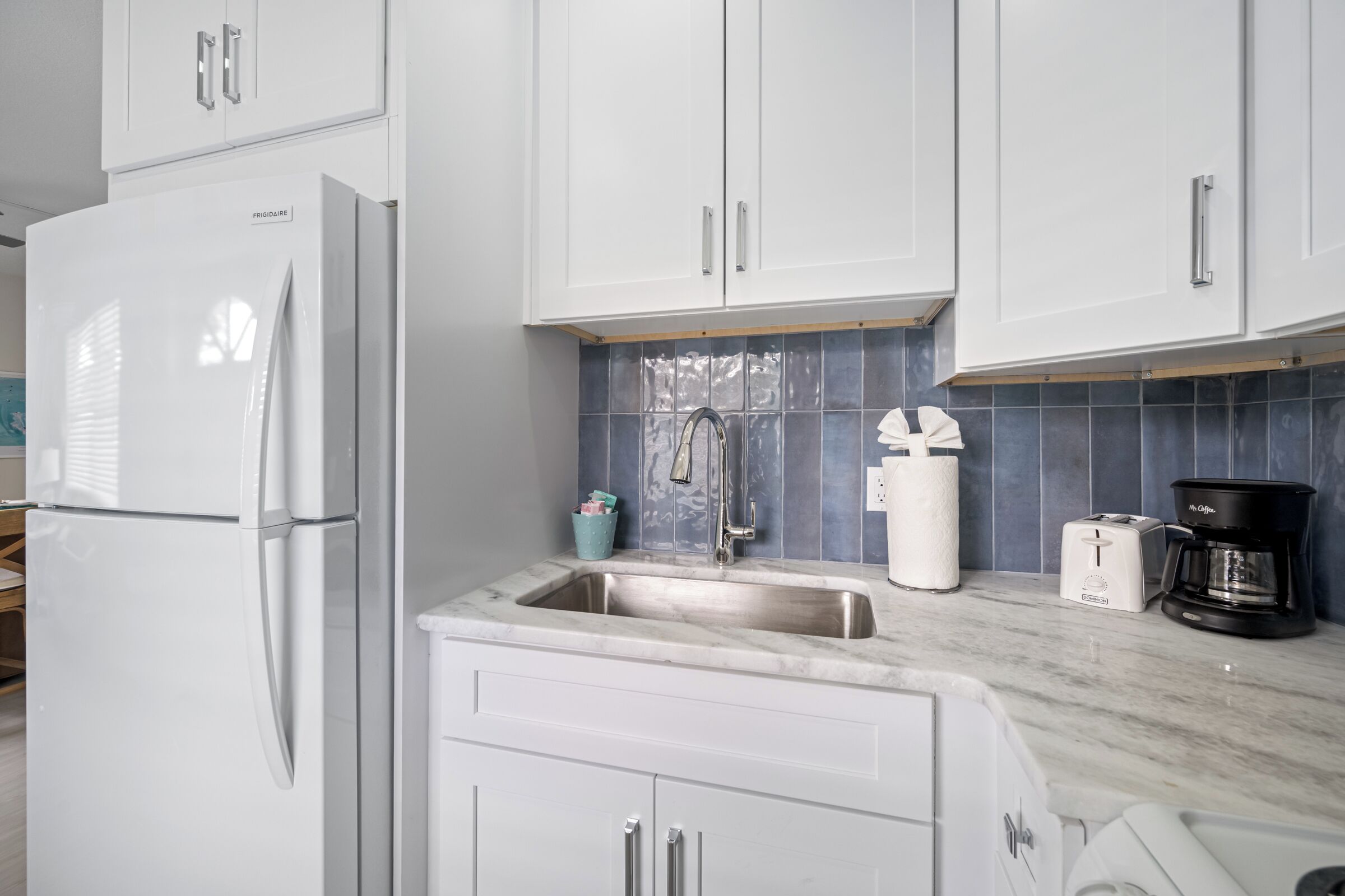 A kitchen with white cabinets, a stainless steel sink, a white refrigerator, a coffee maker, and a toaster.