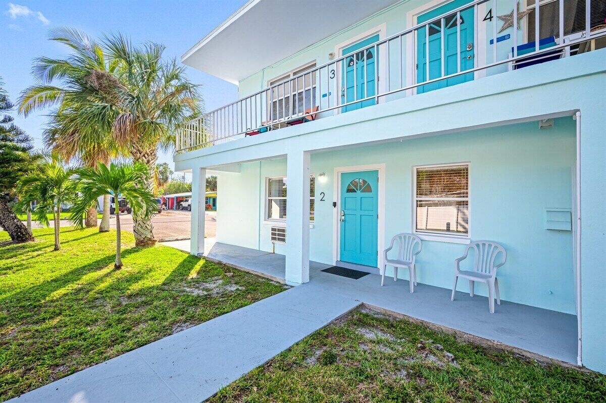 A two-story building with a light blue exterior, numbered doors, and a balcony with white railings.
