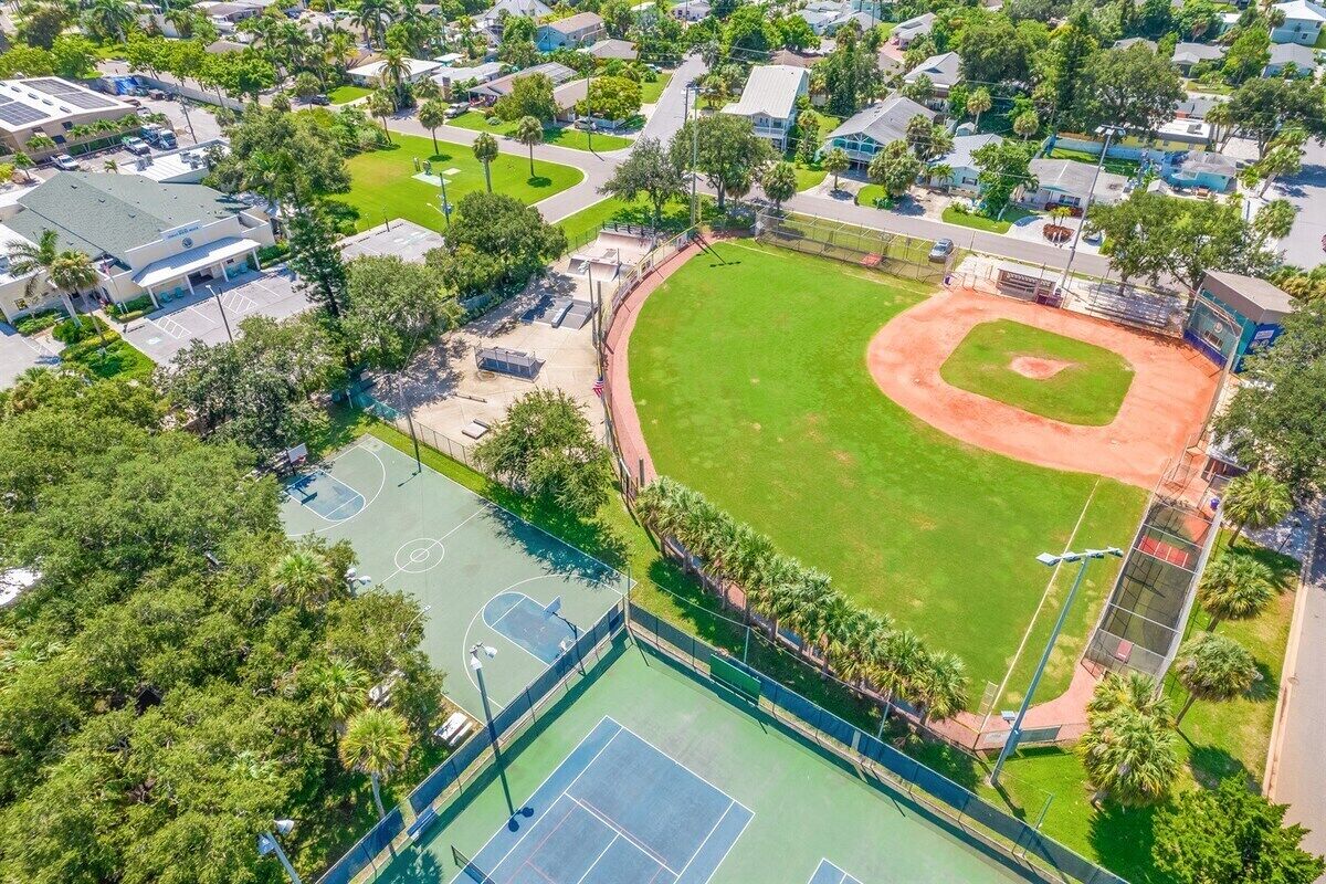 An aerial view of a residential area with a baseball field, tennis courts, and houses.
