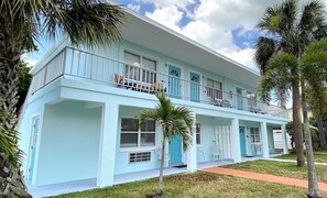 A two-story building with a light blue exterior, balconies, and a covered front porch with chairs.