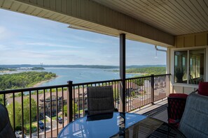 Enjoy breathtaking views of the lake from this balcony, featuring a glass-top table and comfortable seating for two.
