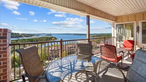 A balcony with a glass table and chairs, overlooking a lake and buildings. - Lakeview Penthouse 4BR/4BA Condo • Sleeps 12 • Sunroom + Balcony (Branson)