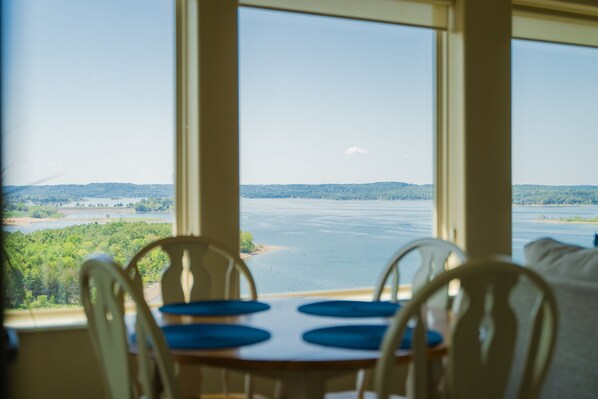Enjoy a meal with a view of the serene lake or river from this dining area, featuring a table for four and a clear view of the surrounding landscape.