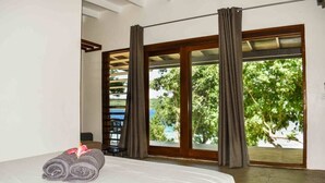 Una habitación de hotel con cama, ventana con cortinas y vistas a la vegetación.