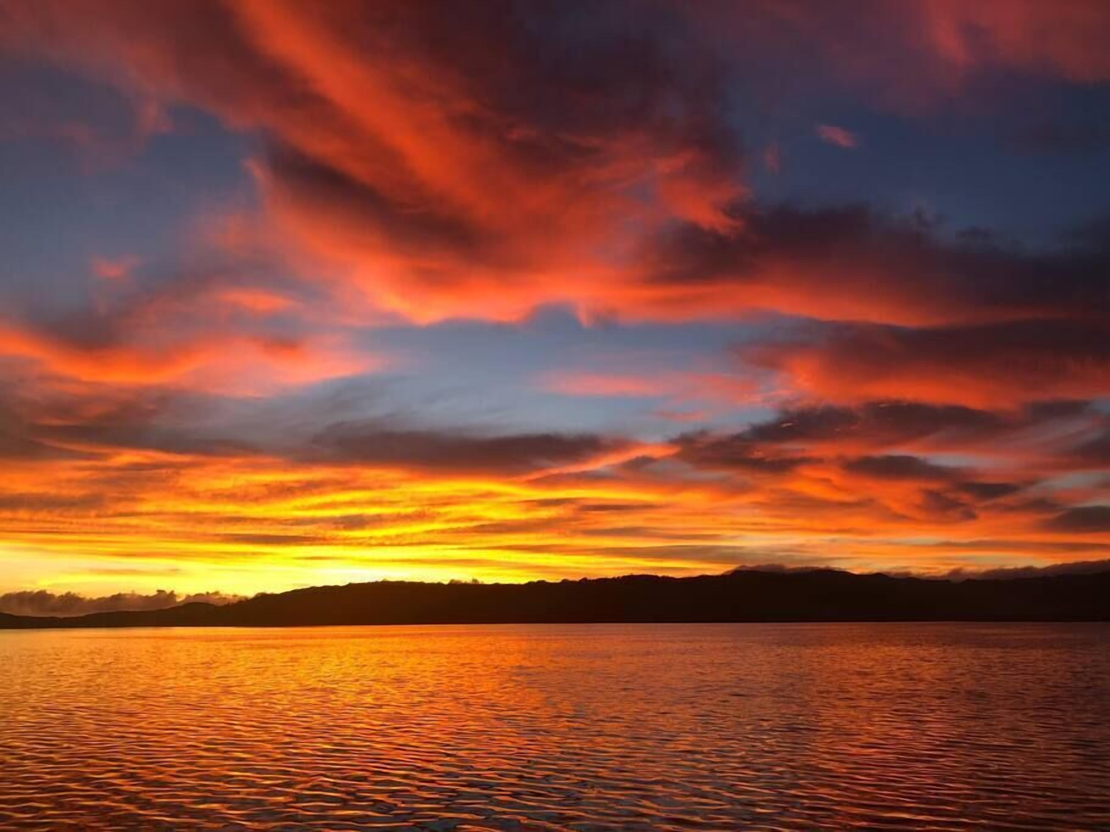 Ein Sonnenuntergang über ruhigem Wasser, im Hintergrund die Silhouette eines Landabschnitts.