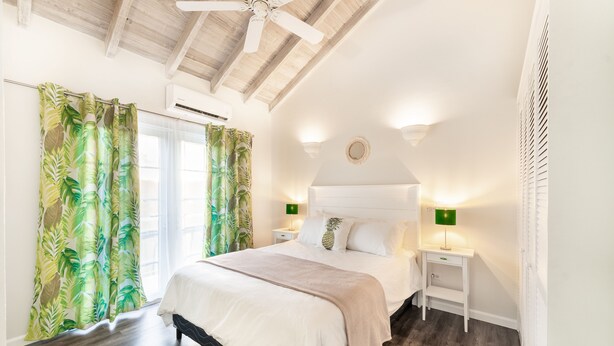 Ein Schlafzimmer mit Bett, Holzboden, Deckenventilator, Nachttisch und Wandlampe.
