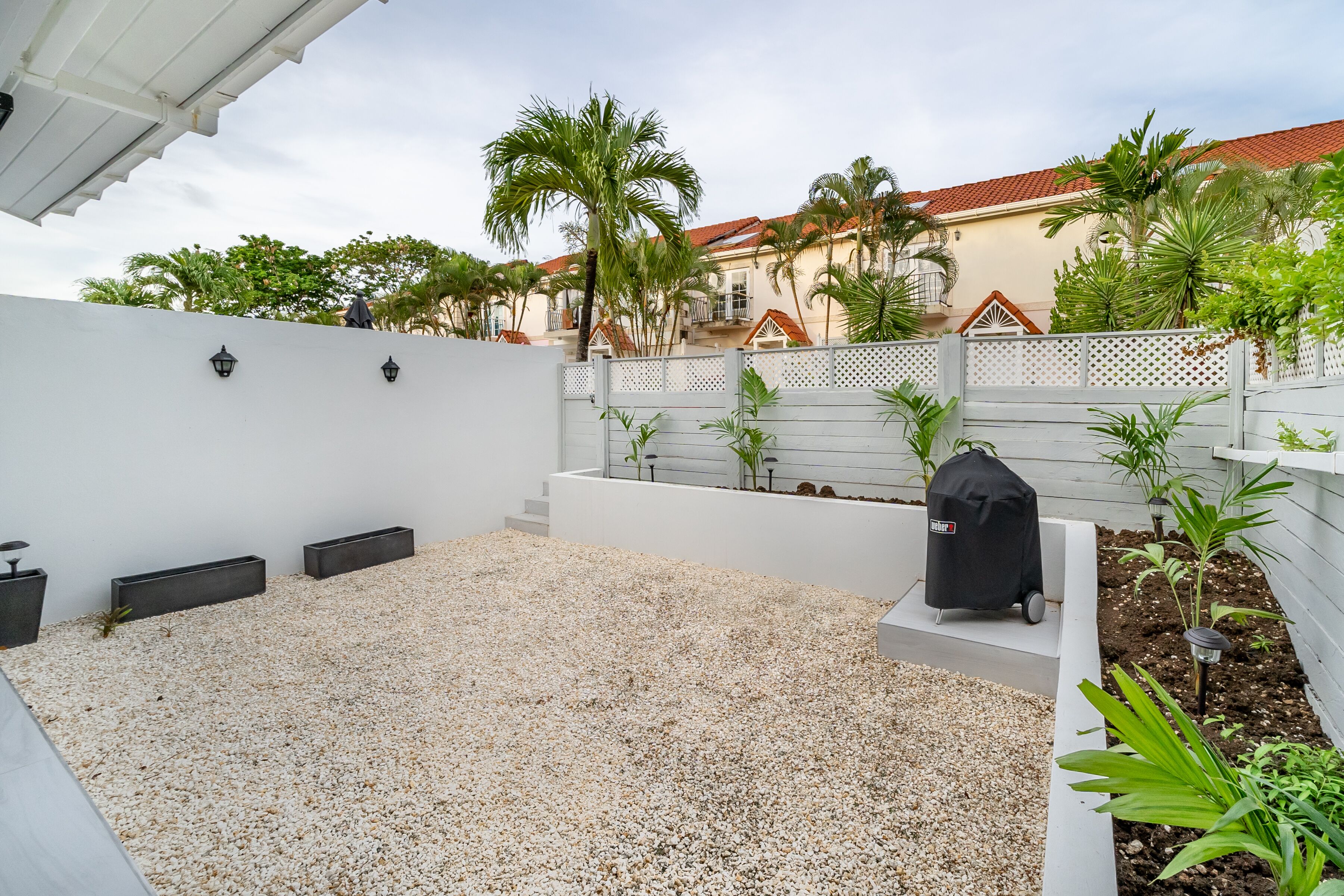 Une terrasse avec un mur blanc, un barbecue et des plantes en pot.