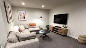 Una sala de estar moderna con un sofá gris, una mesa de centro redonda, un televisor sobre un mueble de madera y una lámpara de pie.