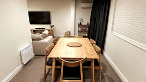 Un comedor con una mesa y sillas de madera, un sofá, un televisor y una ventana con persianas.