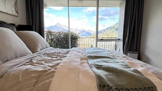 Una cama grande con vistas a montañas desde un balcón.