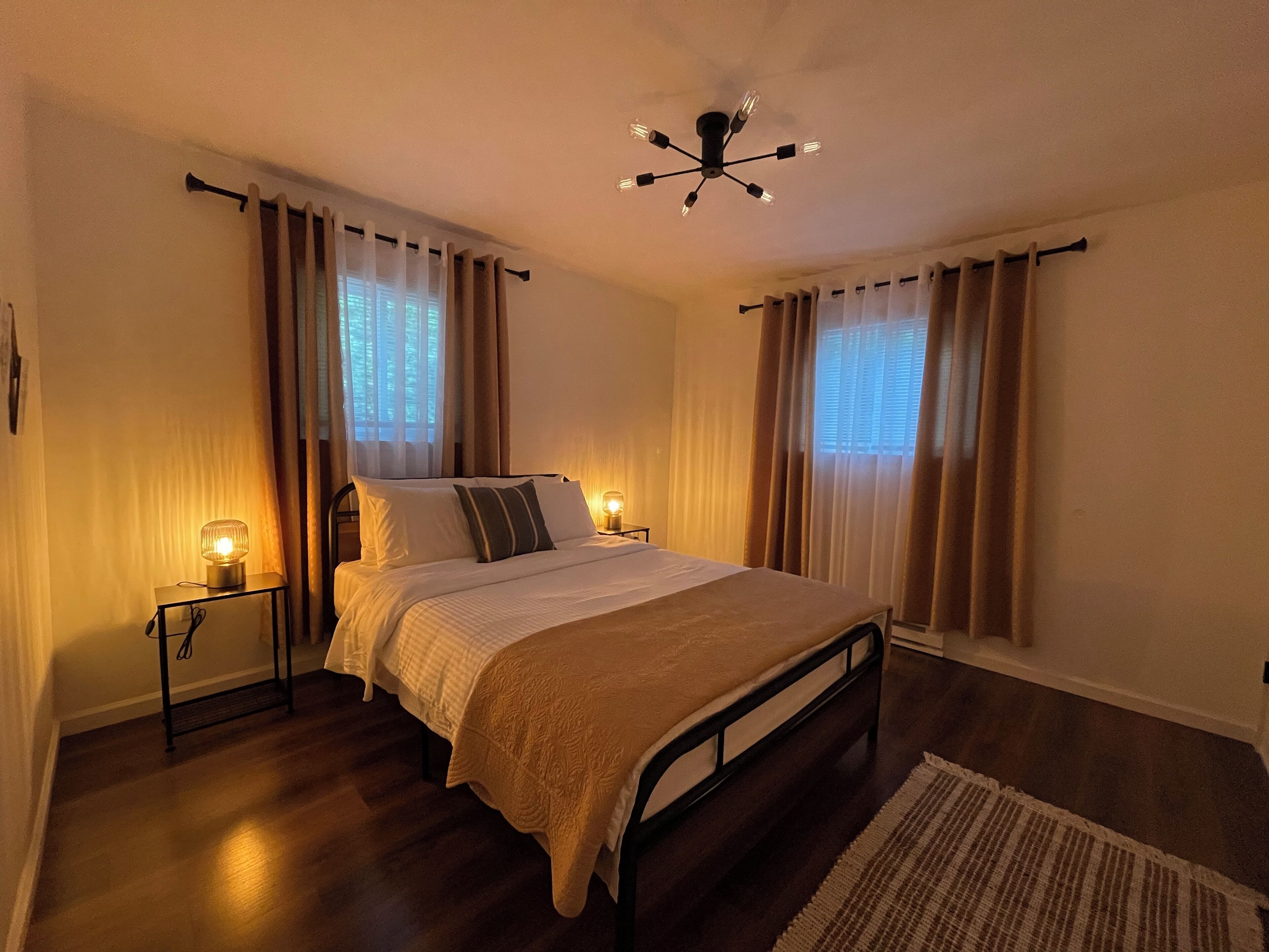 A bedroom with a bed, bedside lamps, a ceiling fan, and curtains.