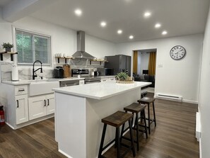 A modern kitchen with a central island, bar stools, and a dining area with a sofa and a coffee table.