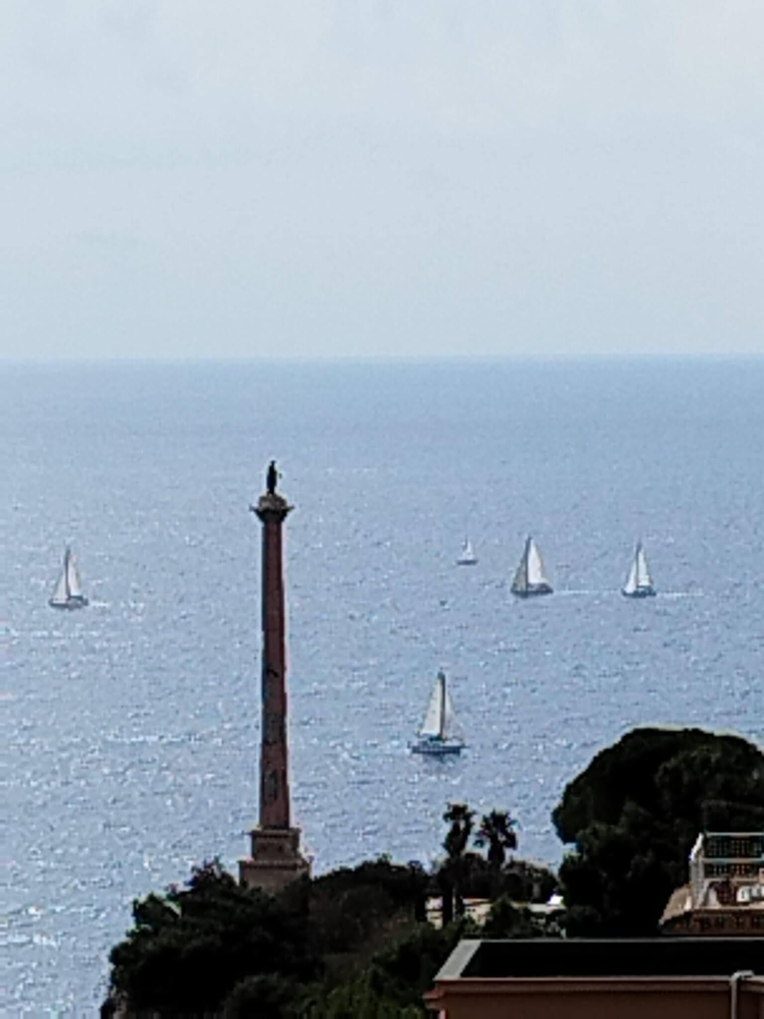 A coastal view with a prominent lighthouse and sailboats on the water.
