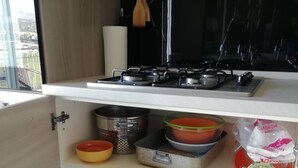 Une cuisine équipée d’une cuisinière à gaz, de différents ustensiles de cuisine et d’une fenêtre donnant sur un paysage urbain.